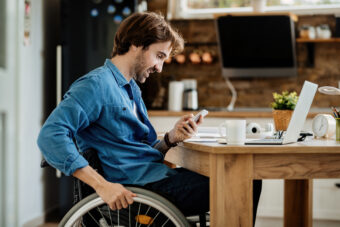 10 young-happy-entrepreneur-wheelchair-reading-message-smart-phone-while-working-home